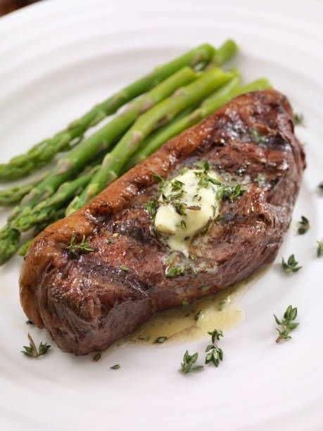 Grilled steak with herb butter and asparagus on a white plate