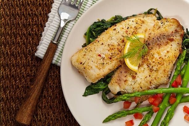 Grilled fish fillets with lemon garnish on a plate with green beans and spinach