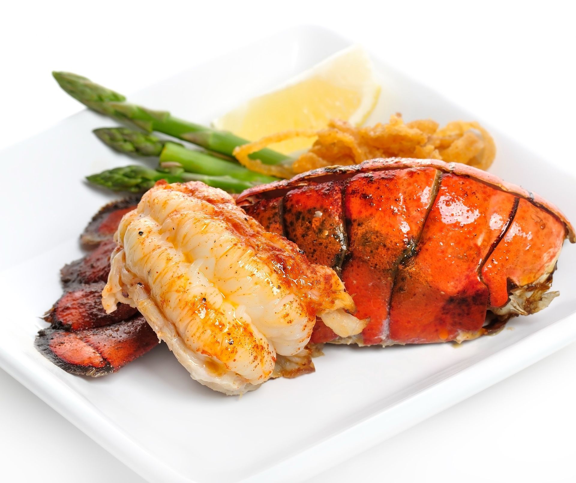 Plated lobster tail with asparagus, fries, and lemon butter on a white dish