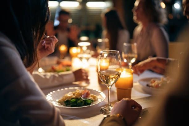 People dining at a warmly lit restaurant table with candles, wine glasses, and plated meals