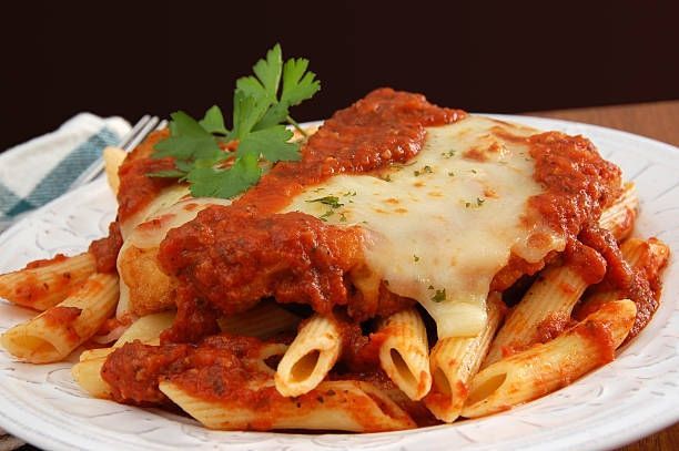 Plate of penne pasta with red marinara sauce, melted cheese, and parsley garnish