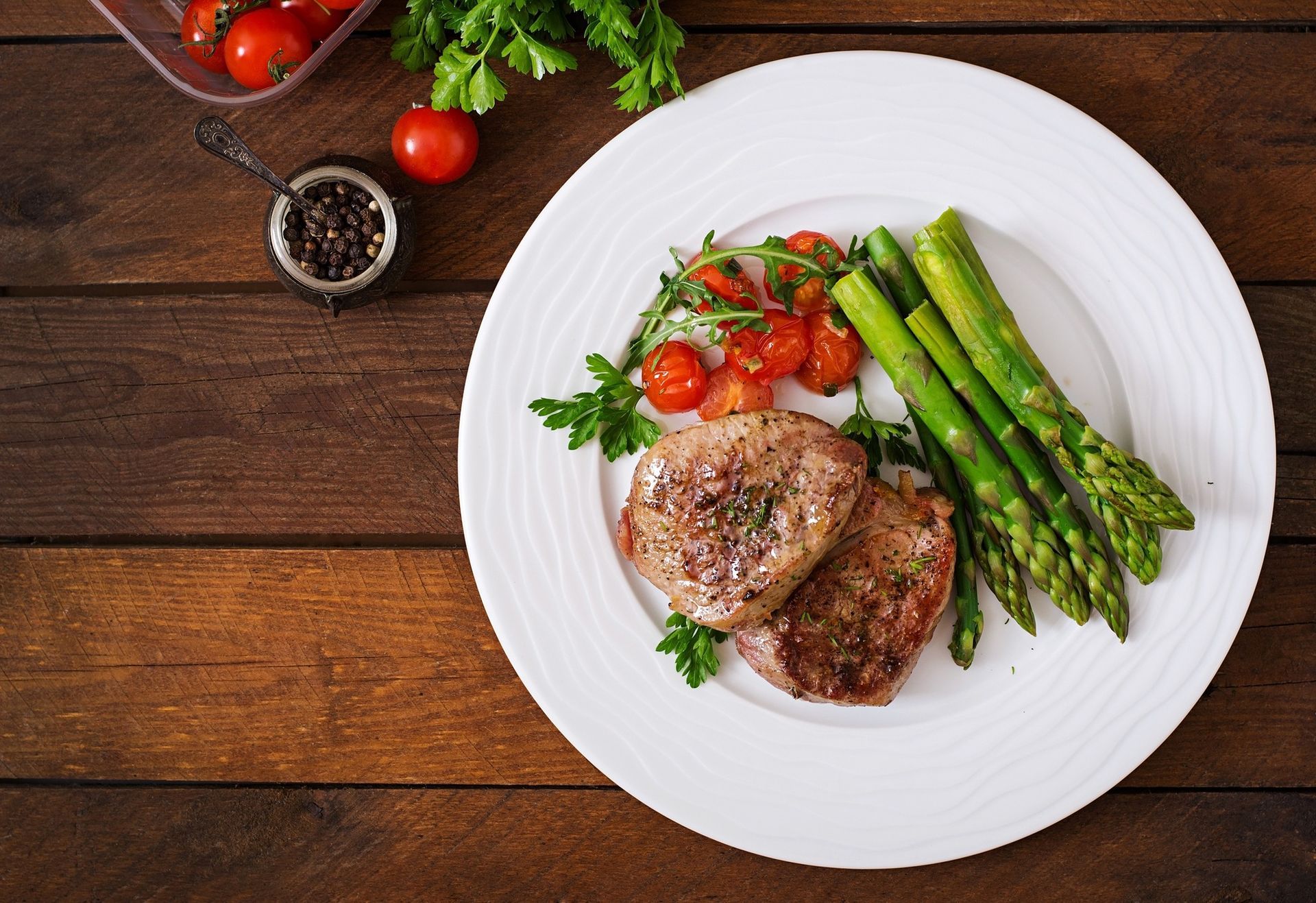 Grilled steak with asparagus and cherry tomatoes on a white plate atop a wooden table