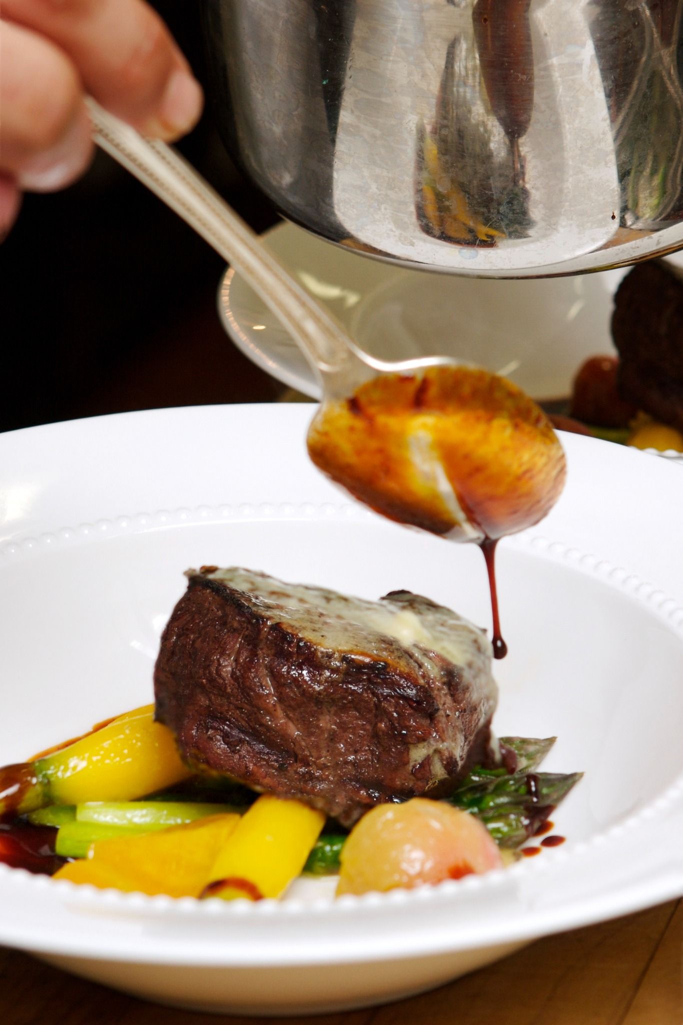 Chef plating a seared steak with vegetables and sauce on a white plate