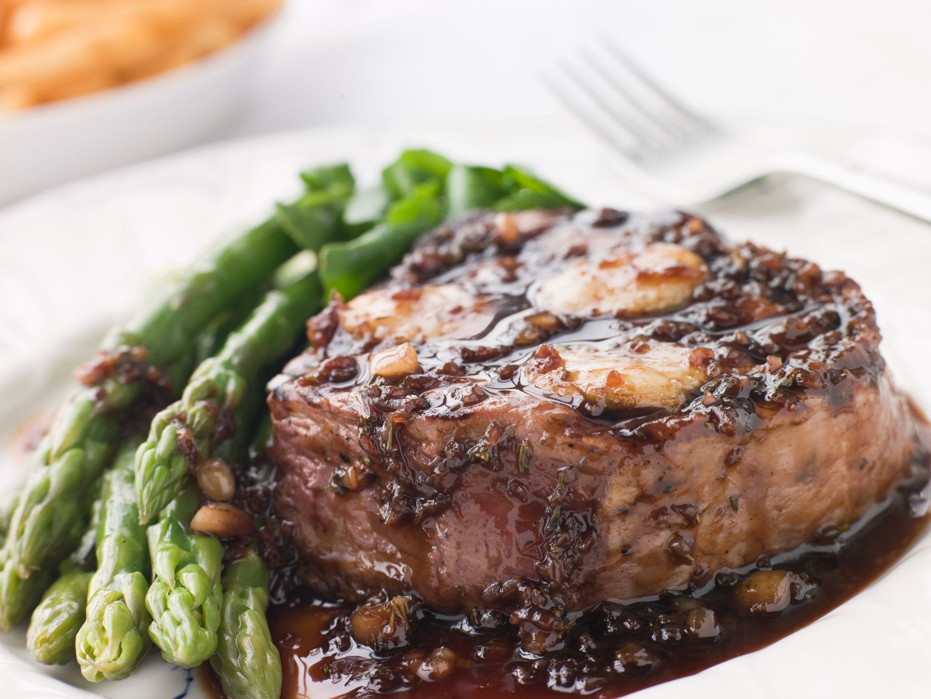 Grilled steak medallion with asparagus spears on a white plate, topped with melted butter and sauce