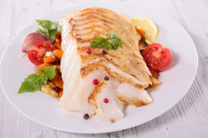Grilled fish fillet with cherry tomatoes, herbs, and lemon on a white plate