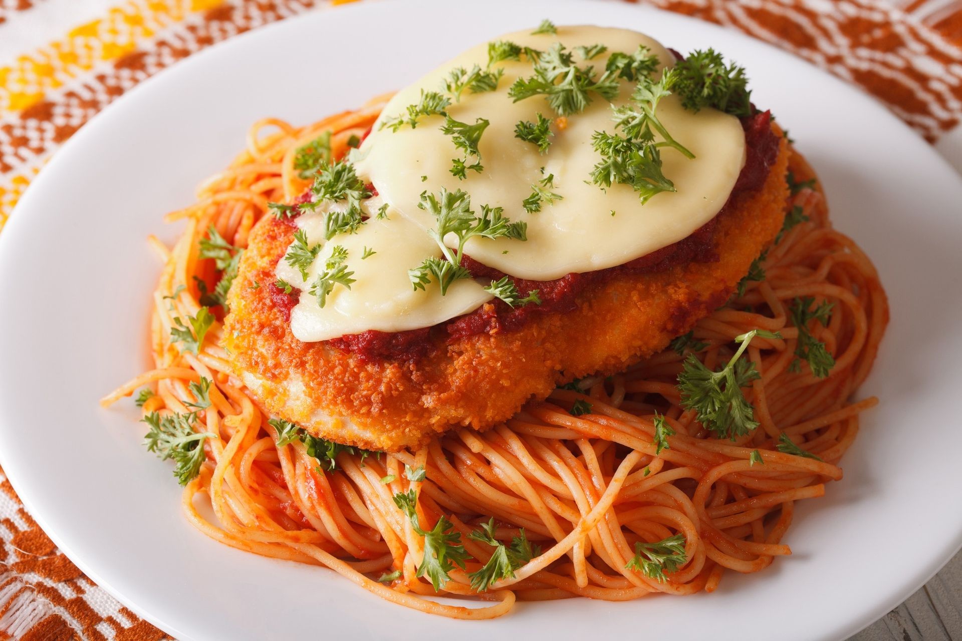 Breaded chicken cutlet on spaghetti with melted cheese and herbs on a white plate