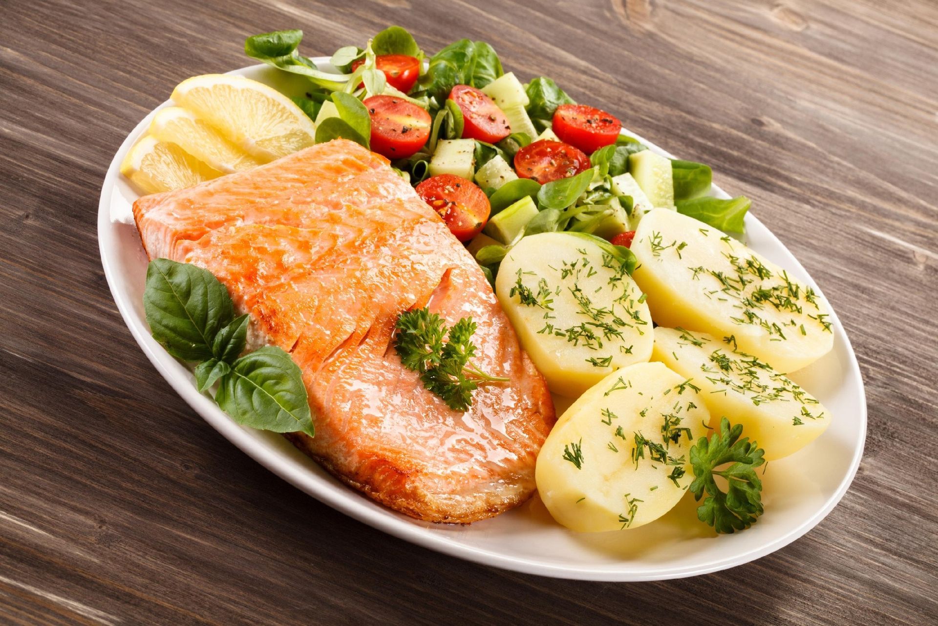 Salmon fillet with potatoes, lemon, and cherry tomato salad on a white plate