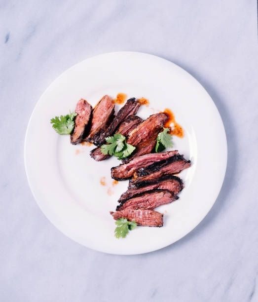 Plated sliced grilled meat garnished with herbs on a white plate