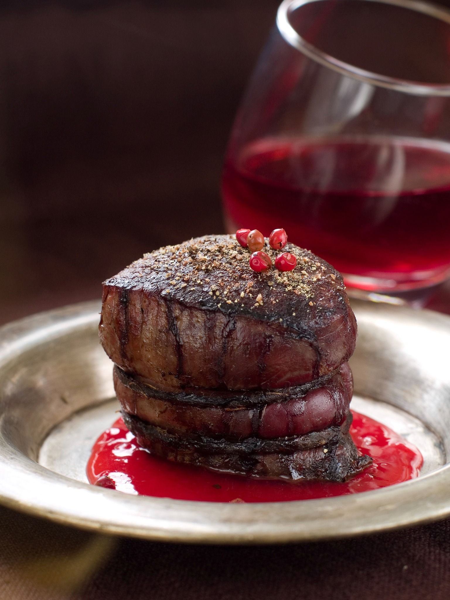 Chocolate dessert topped with berries on a plate, with red sauce and a glass of red wine behind it