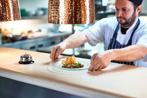 Chef plating a gourmet dish on a white counter in a modern restaurant kitchen