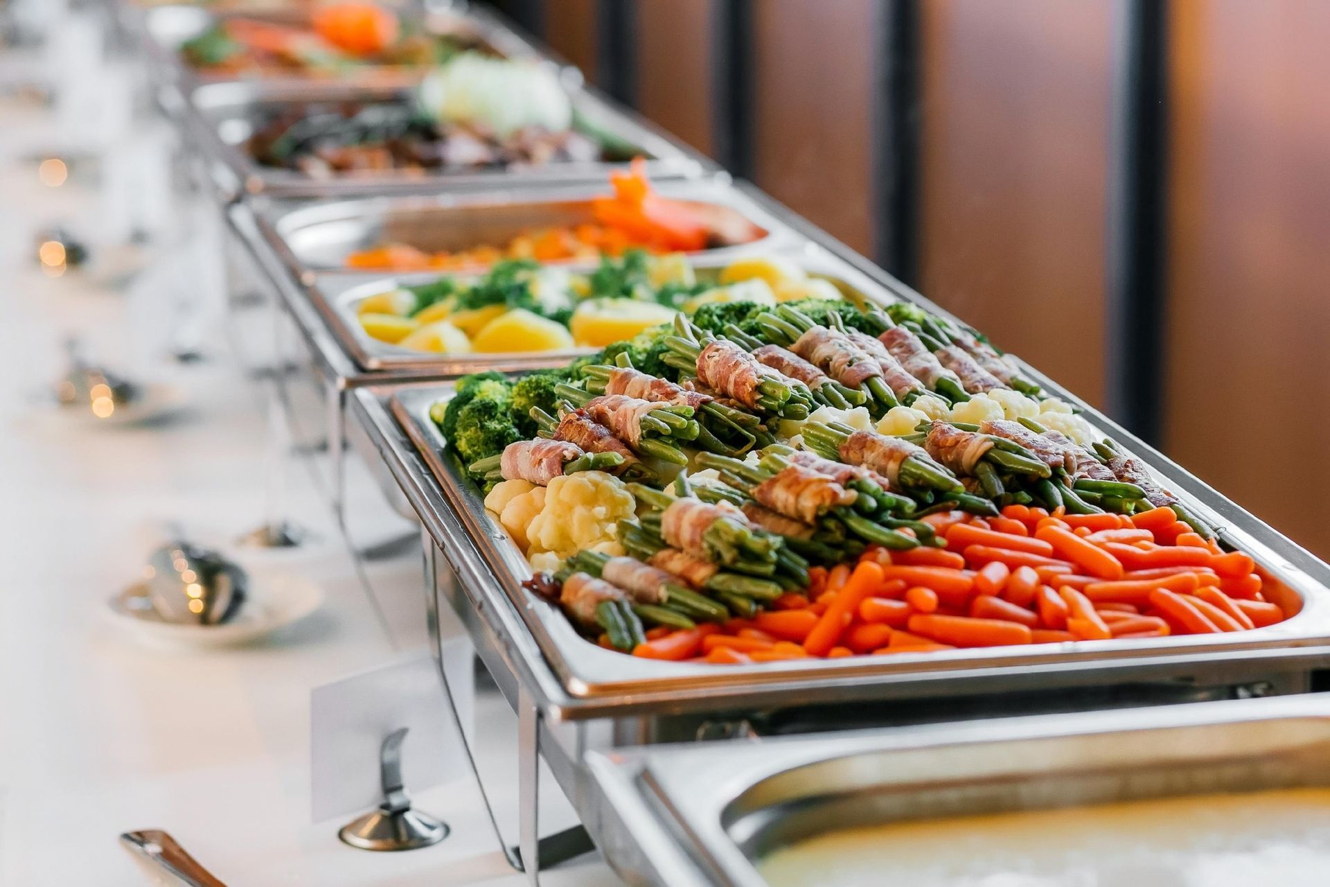 Buffet line with trays of mixed salads and vegetables on a white table runner