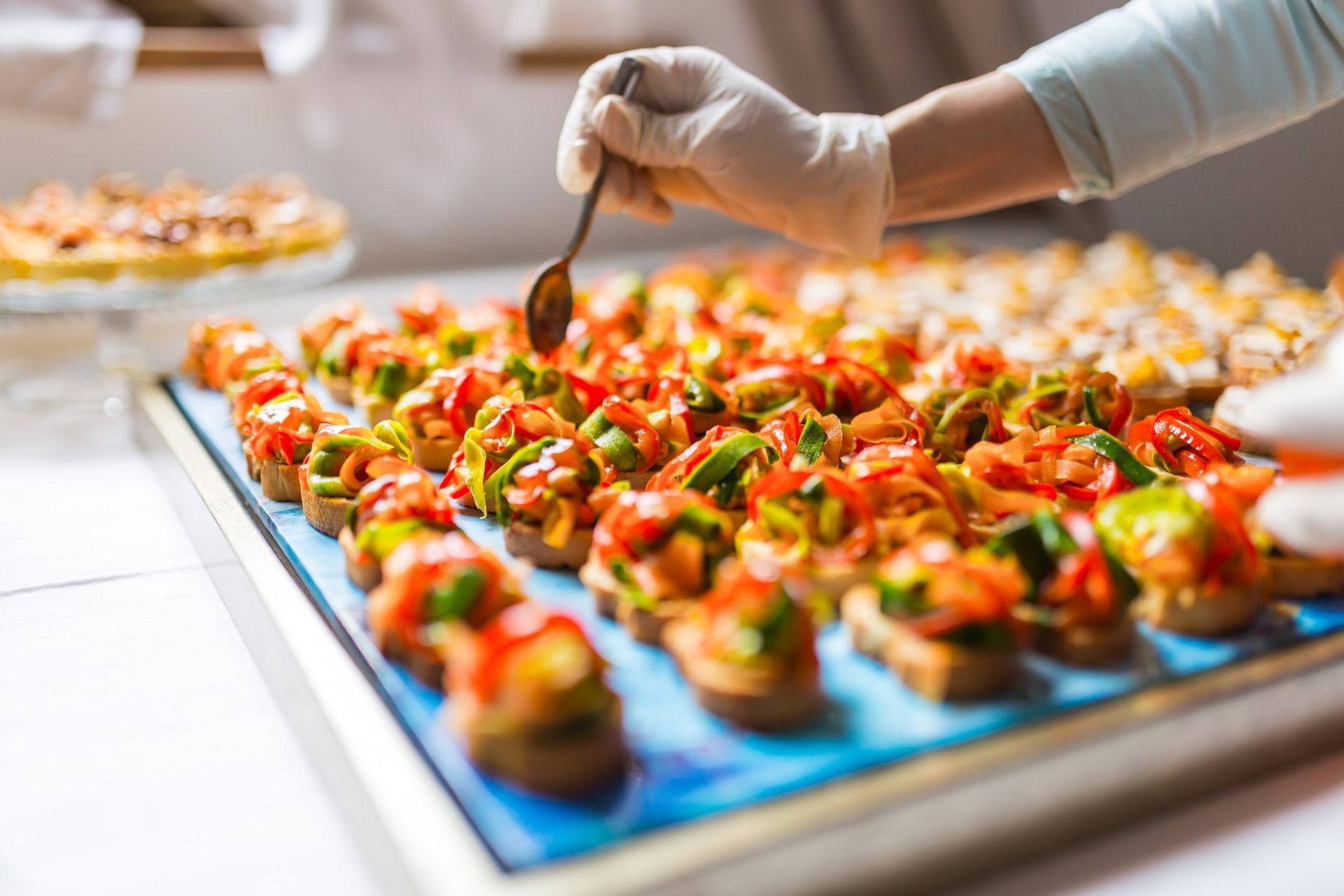 Gloved hand arranging colorful appetizers on a serving tray in a catering kitchen