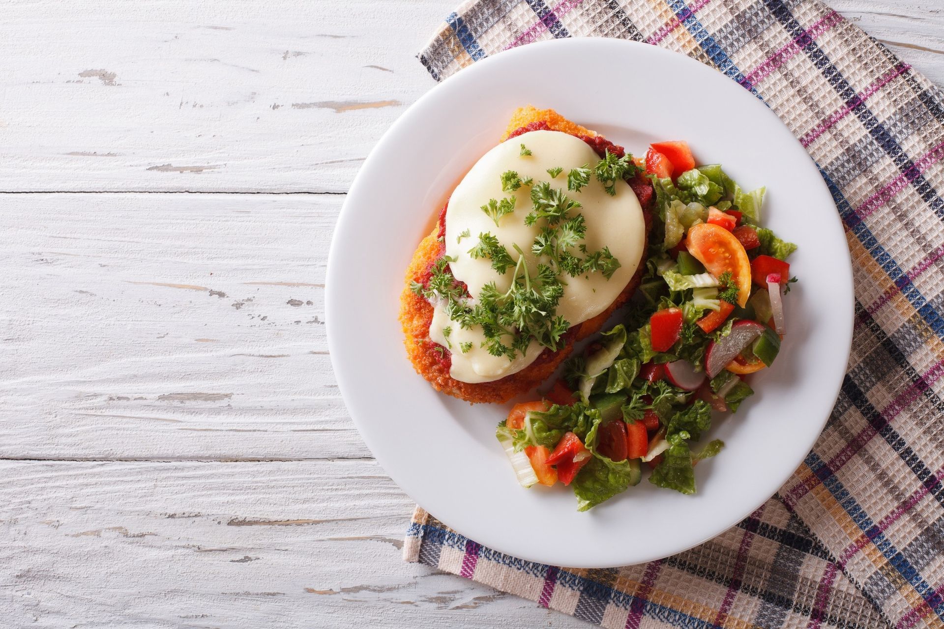 Plated poached eggs with greens and cherry tomatoes on a white dish over a plaid napkin
