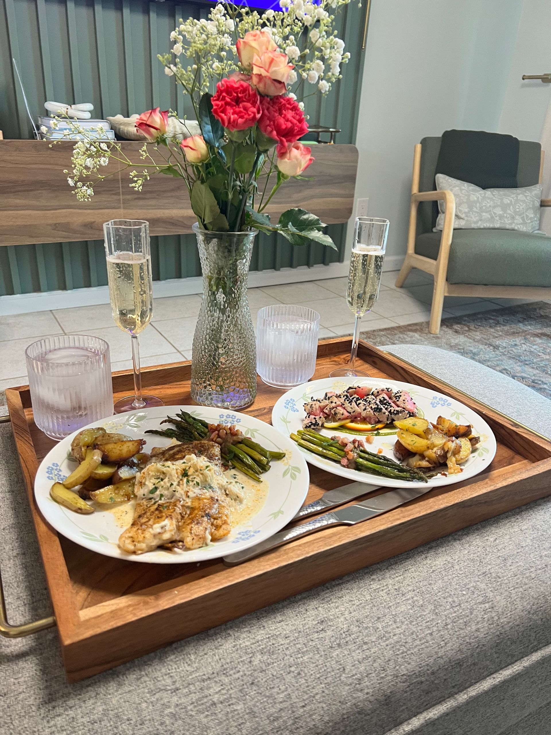 Breakfast tray on a sofa table with two plates of food, champagne glasses, and a vase of flowers