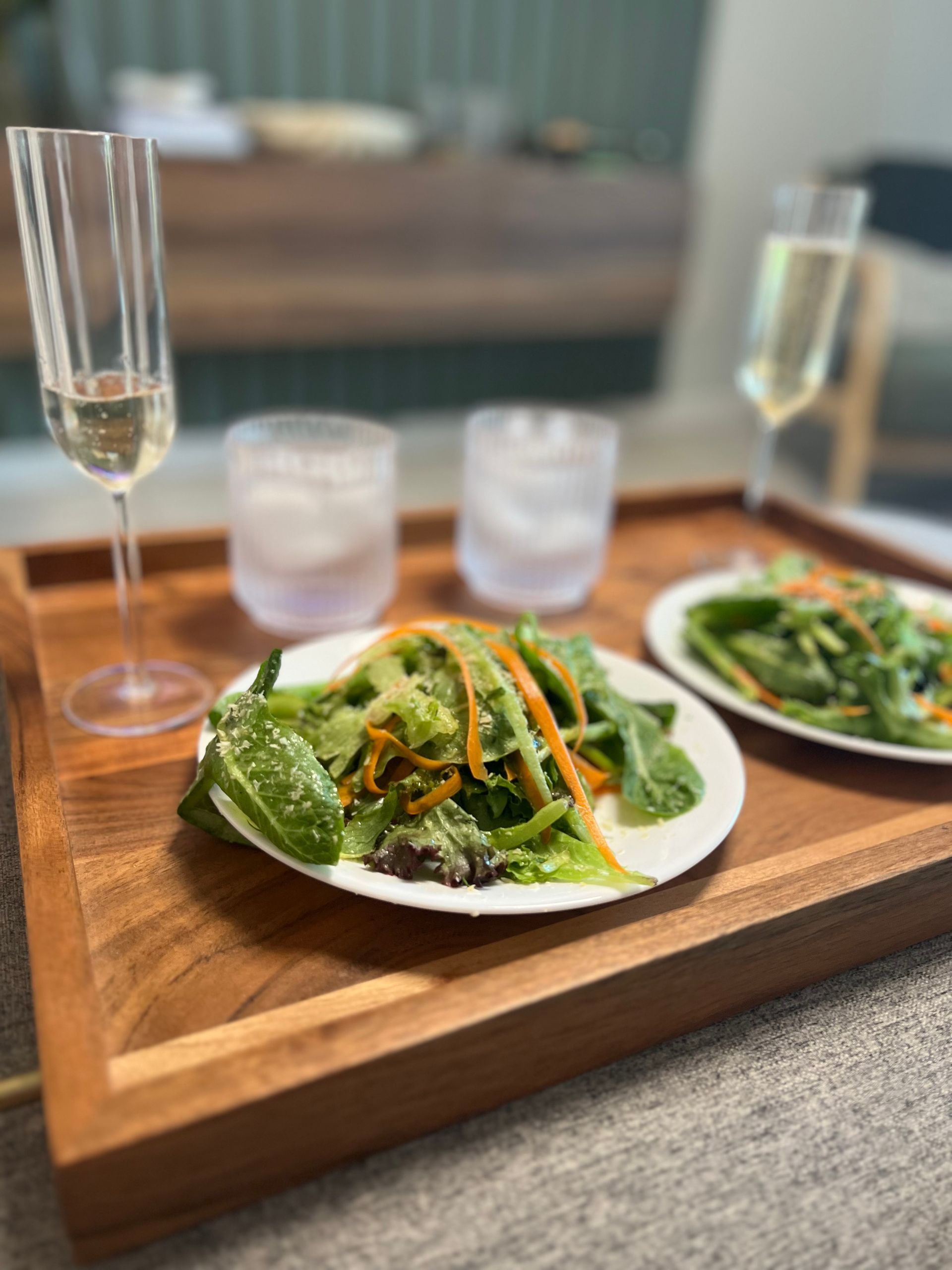 Salad on a wooden tray with drinks and glasses on a table in a restaurant