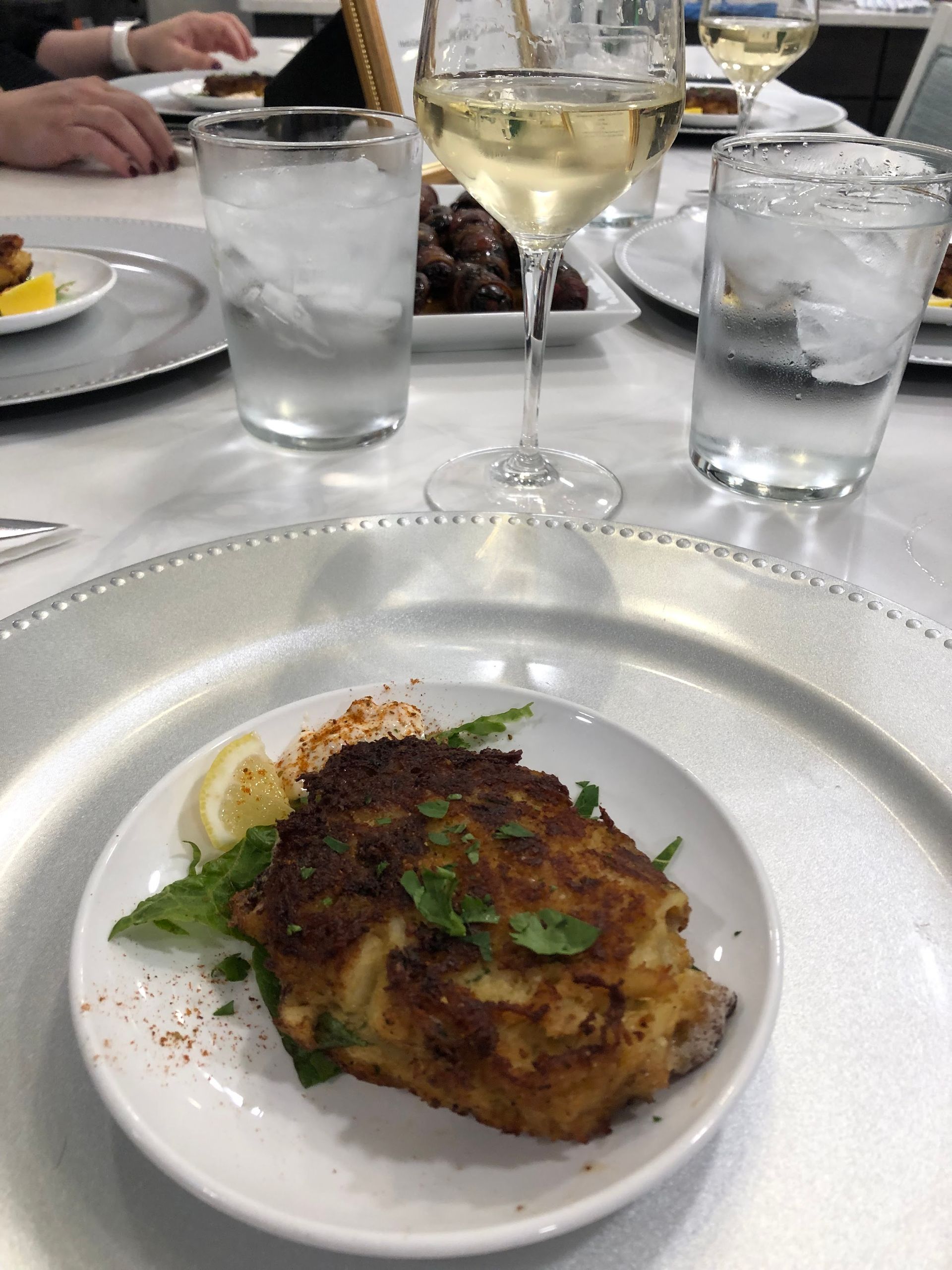 Plated grilled dish with herbs on a restaurant table, with water glasses and a wine glass nearby