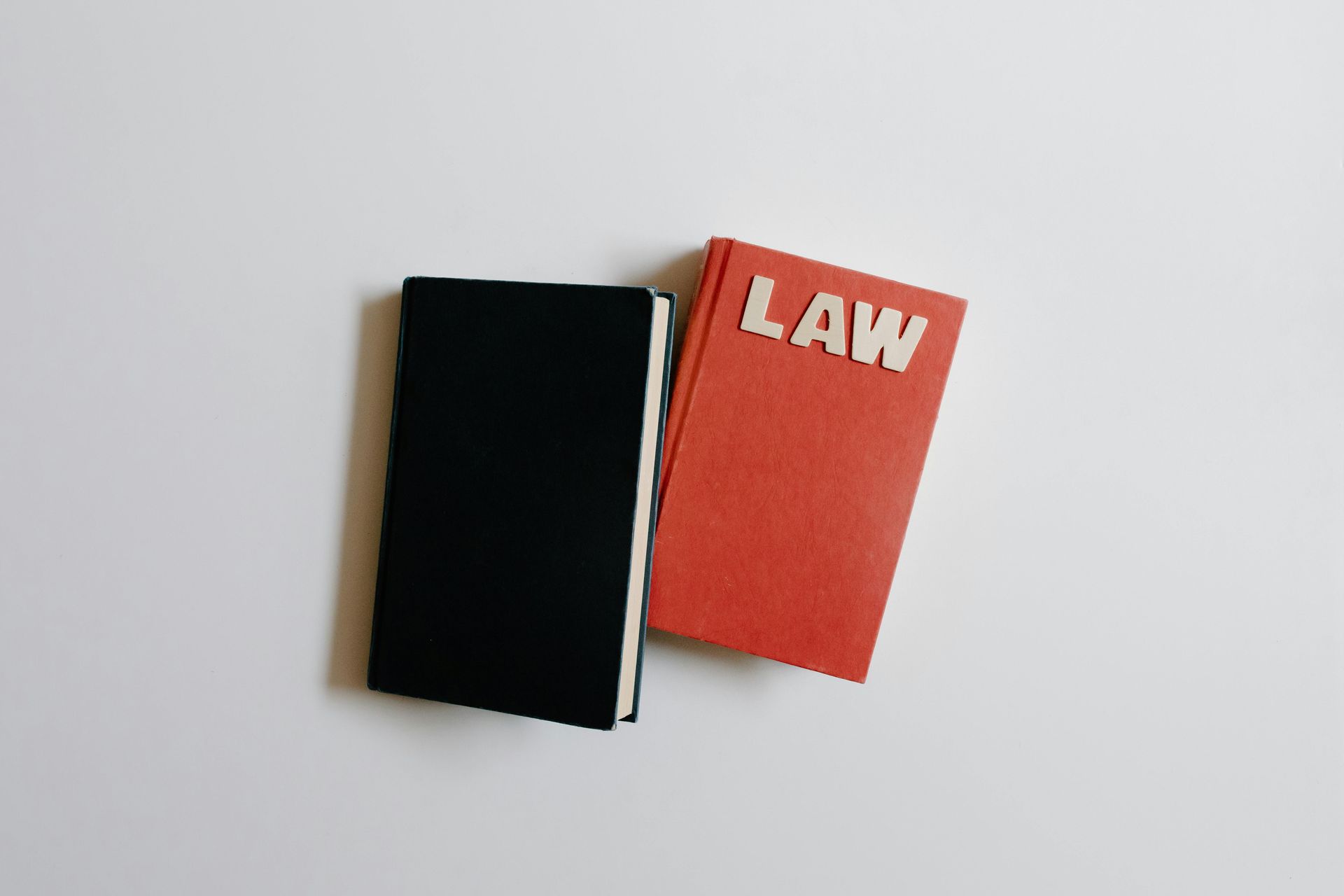 Two small books on a white background, one black and one red labeled “LAW”