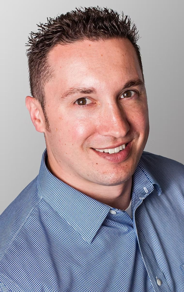 Portrait of a smiling person in a blue button-up shirt against a light gray background