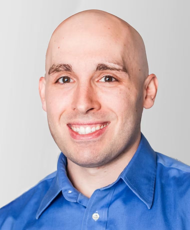 Smiling bald man in a blue button-up shirt against a light gray background