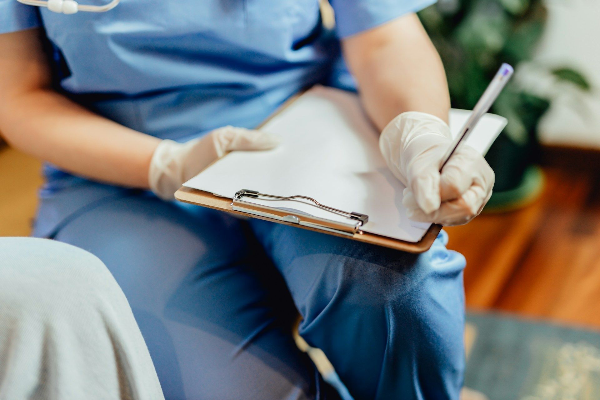 Healthcare worker in blue scrubs and gloves writing on a clipboard