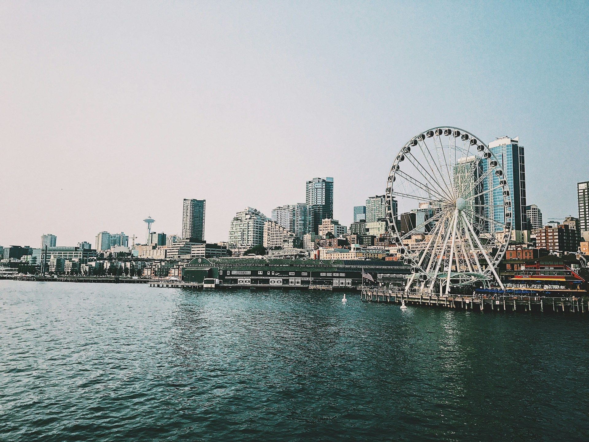 Waterfront city skyline with a large Ferris wheel beside calm water at dusk