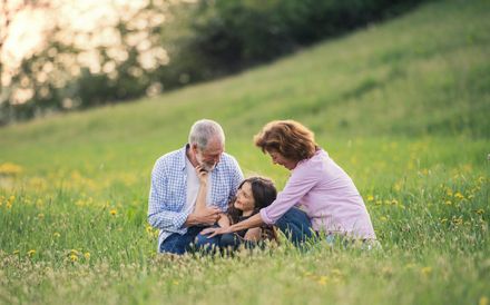 Three people sitting together in a grassy field, looking at something in their hands.