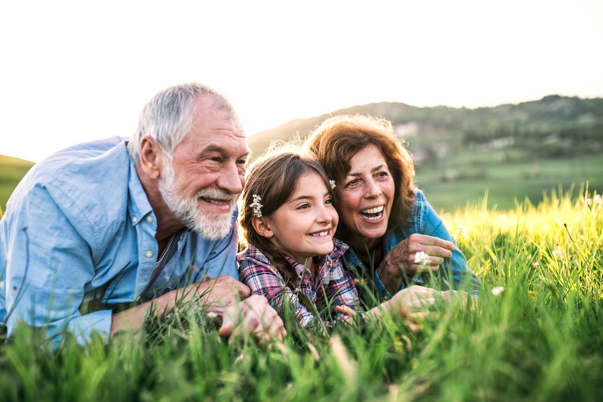 Three people lying in tall grass, smiling in a sunny field at sunset.