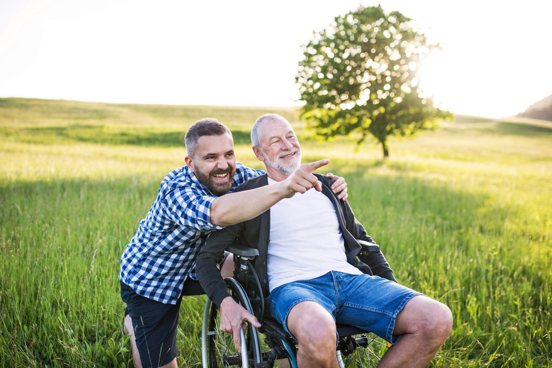 Two people smiling in a wheelchair in a sunny green field