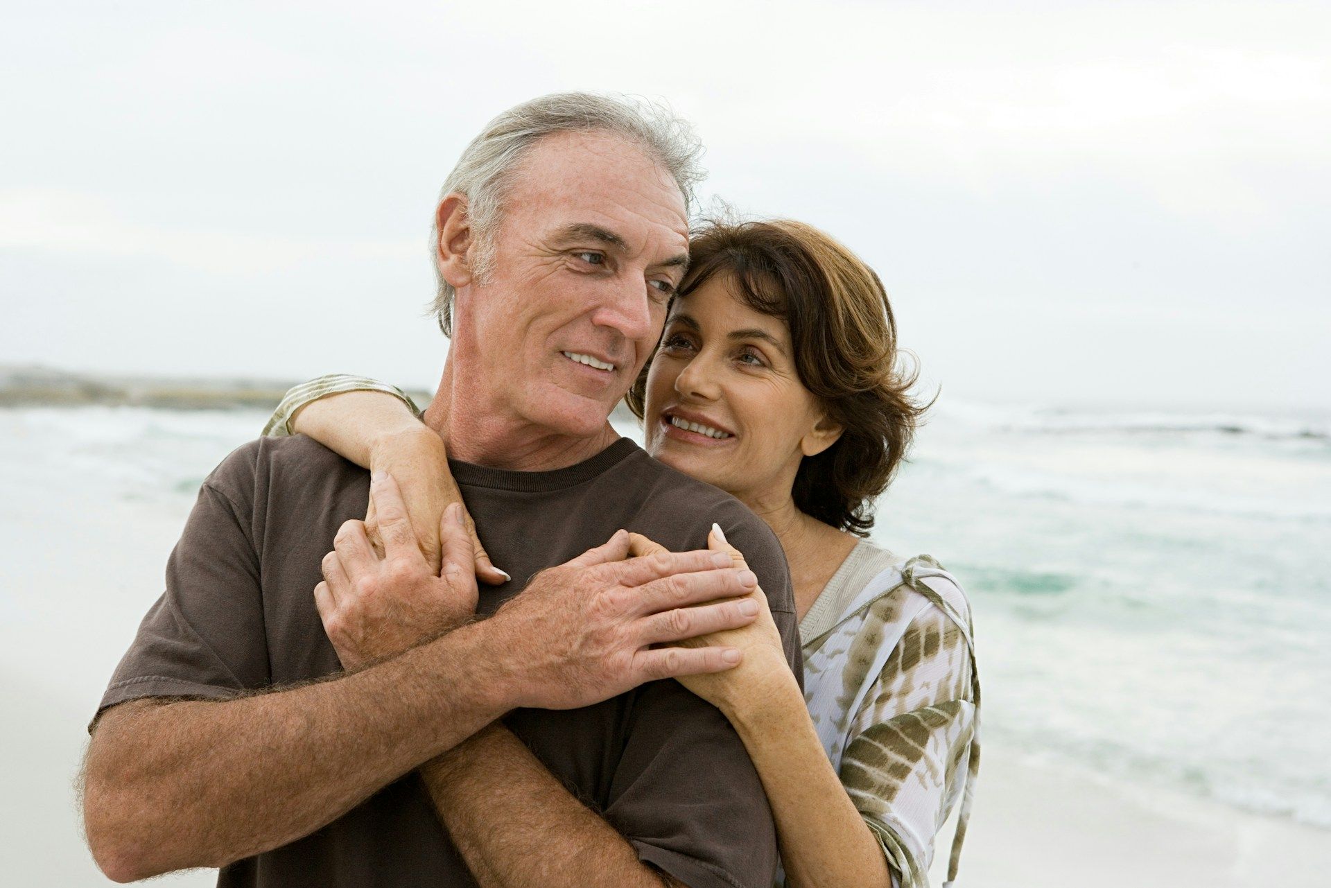 Couple embracing on a beach, smiling with waves in the background