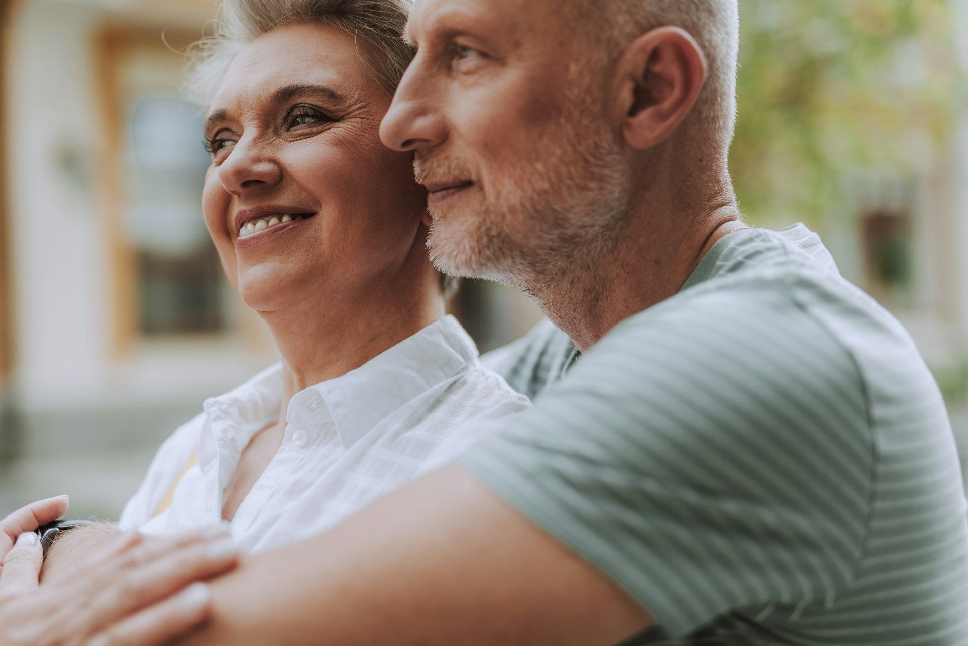 Smiling couple sitting close together outdoors, with a soft blurred background
