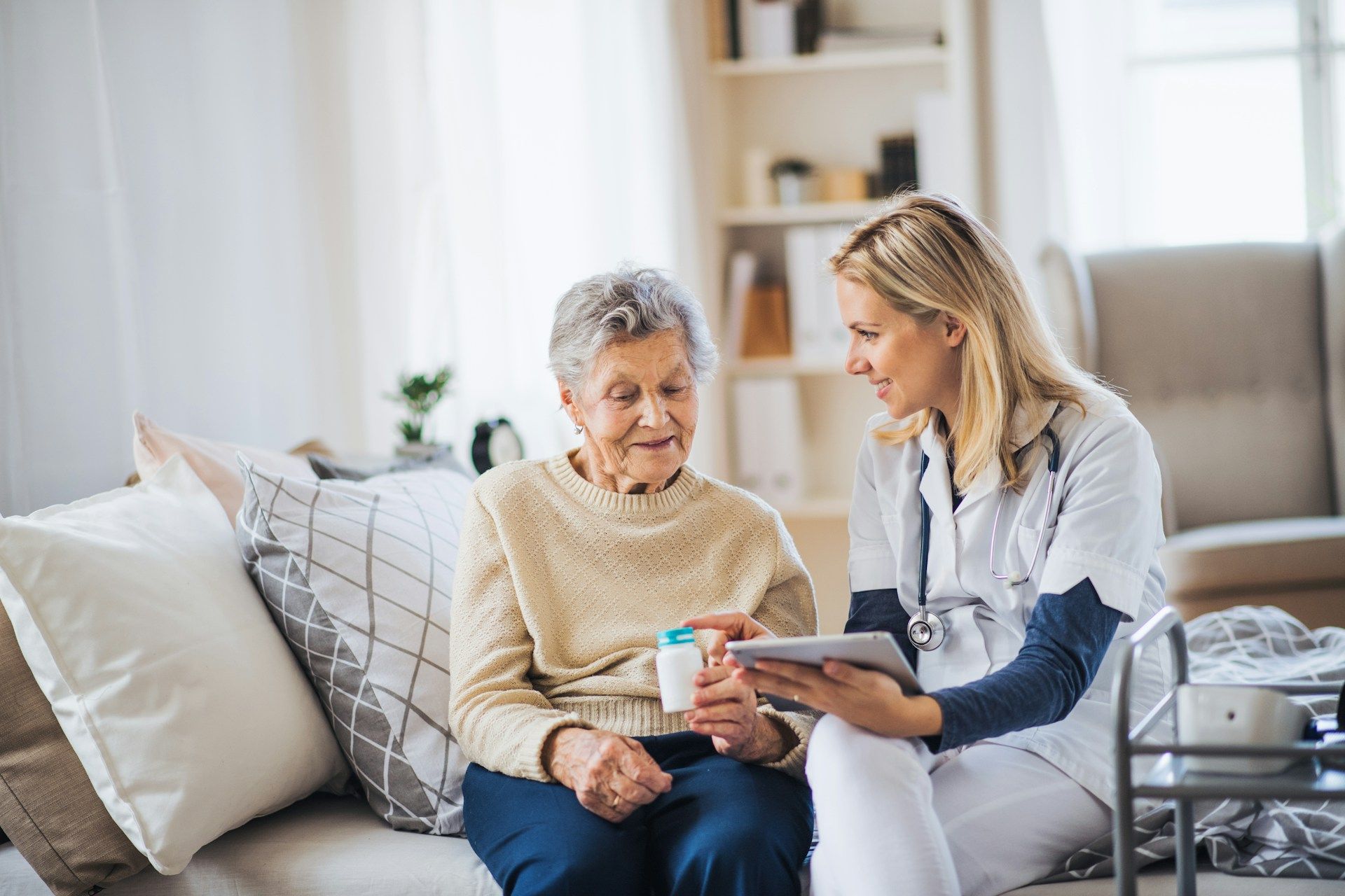 Caregiver showing a tablet to an elderly person on a couch in a bright living room