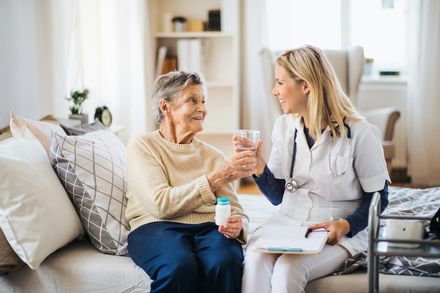 Caregiver and older woman smiling and sharing a drink in a bright living room
