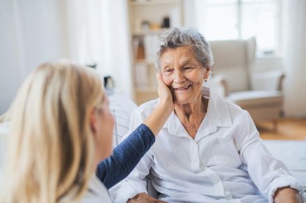 Older woman smiling while a blonde person gently touches her face in a bright living room