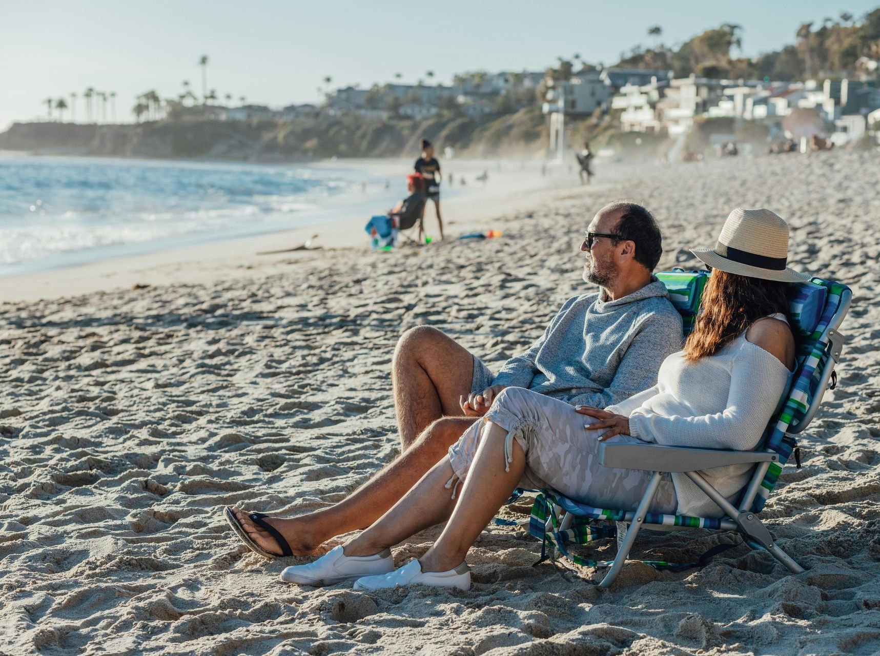 Couple lounging in beach chairs on a sunny sandy beach with ocean waves nearby