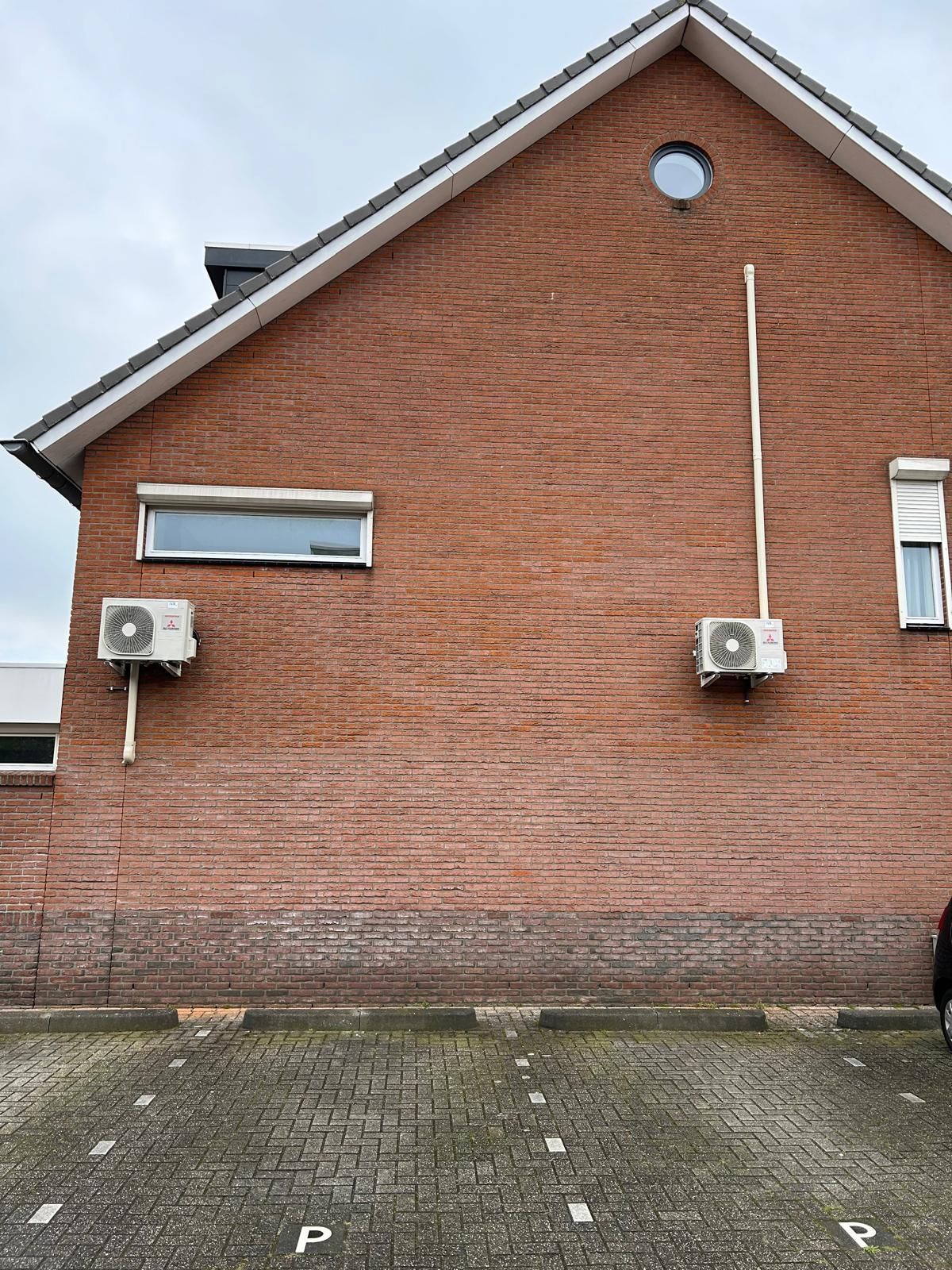 Een rood bakstenen gebouw met airconditioningunits en een klein rond raam.