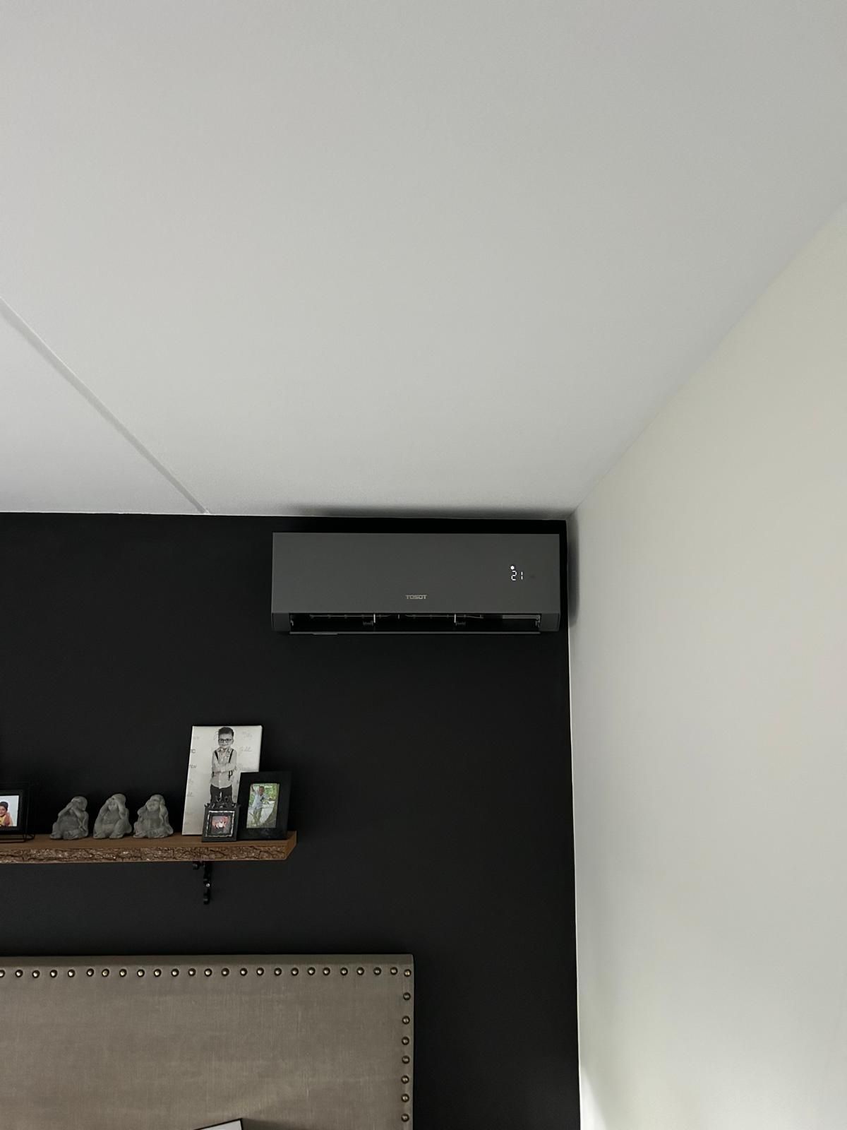 Zwarte wandairco in een slaapkamer. Zwarte muur met plank vol spullen, crèmekleurige muur rechts ervan.