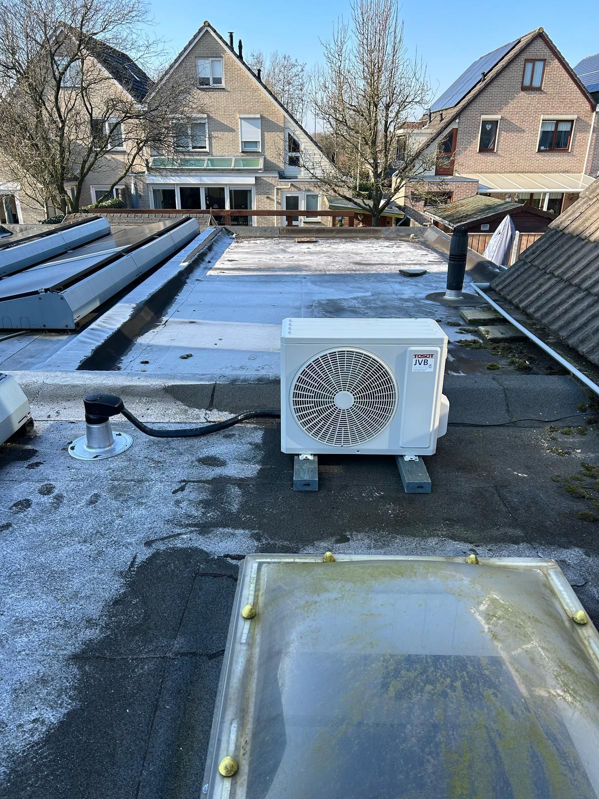 Witte airconditioningunit op een plat dak. Andere gebouwen op de achtergrond onder een blauwe hemel.