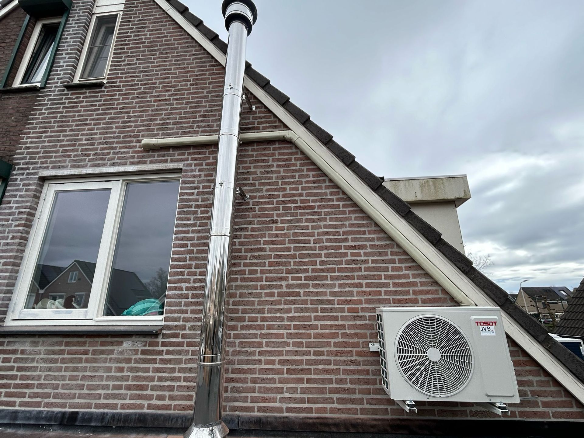Een bakstenen gebouw met een raam, een schoorsteen en een airconditioningunit.