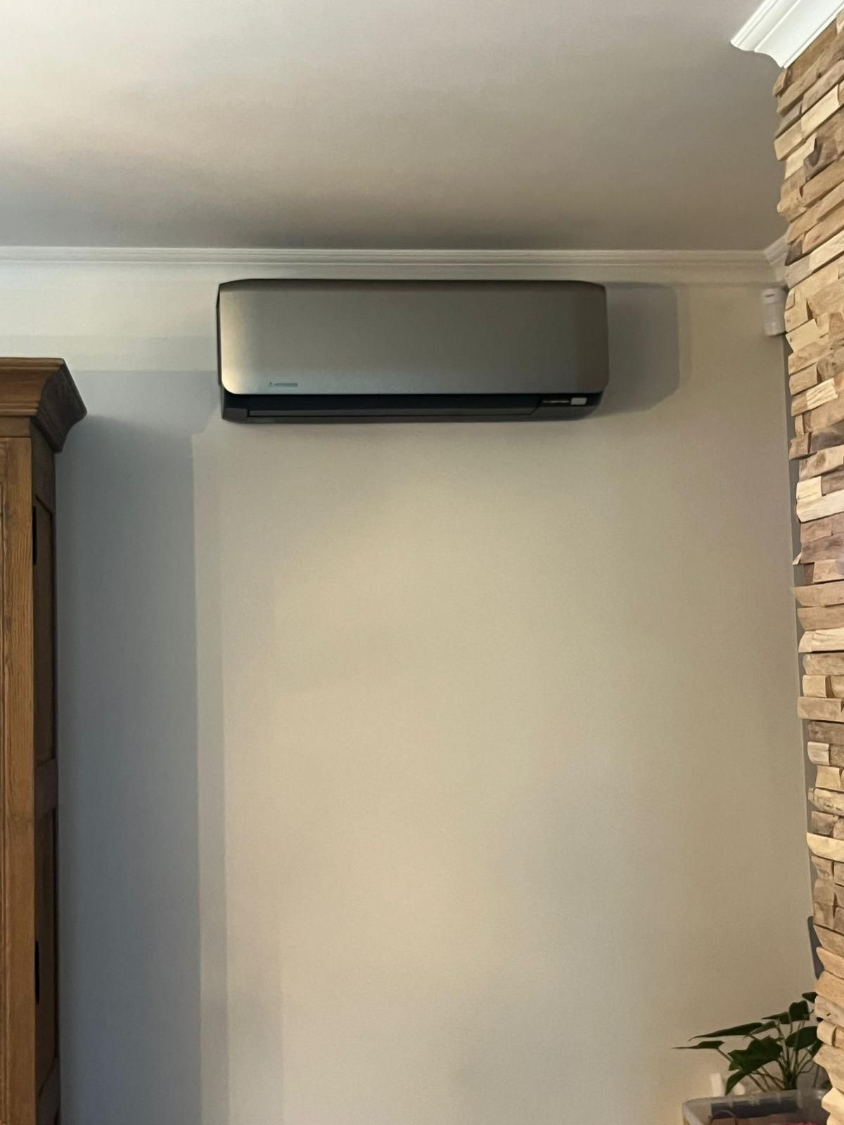 Zilverkleurige airconditioner gemonteerd aan een beige muur, naast een accentmuur van natuursteen.