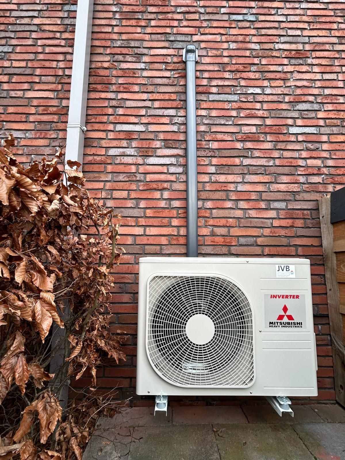 Mitsubishi airconditioningunit gemonteerd op een bakstenen muur met zichtbare leidingen.