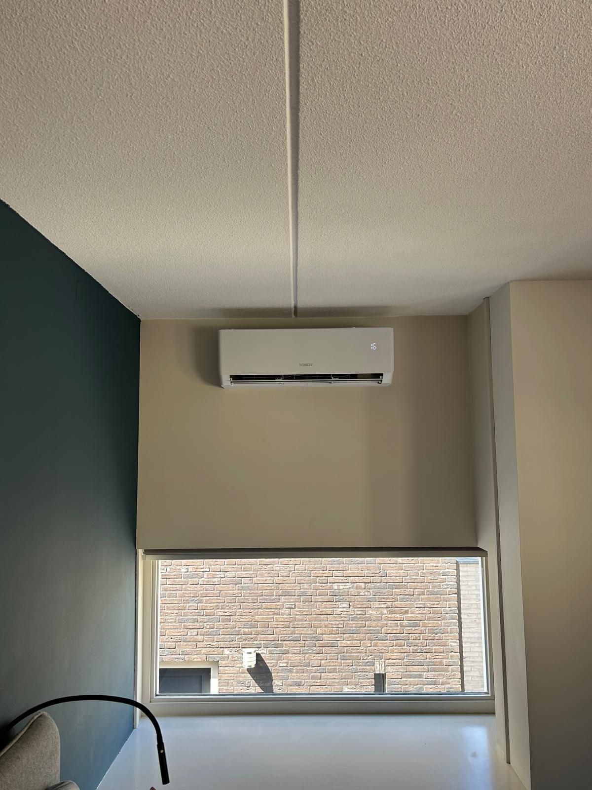Witte airconditioningunit boven een raam in een kamer met een turquoise muur.