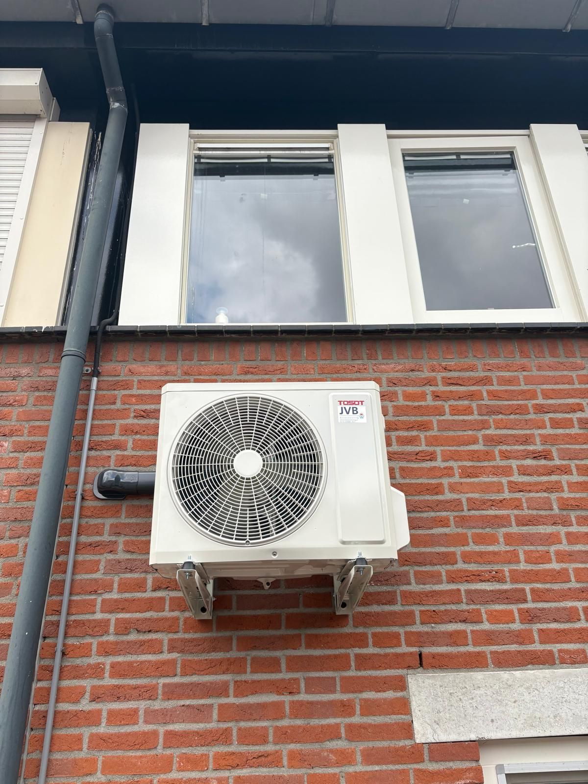 Een airconditioningunit gemonteerd aan een rode bakstenen muur, onder de ramen.
