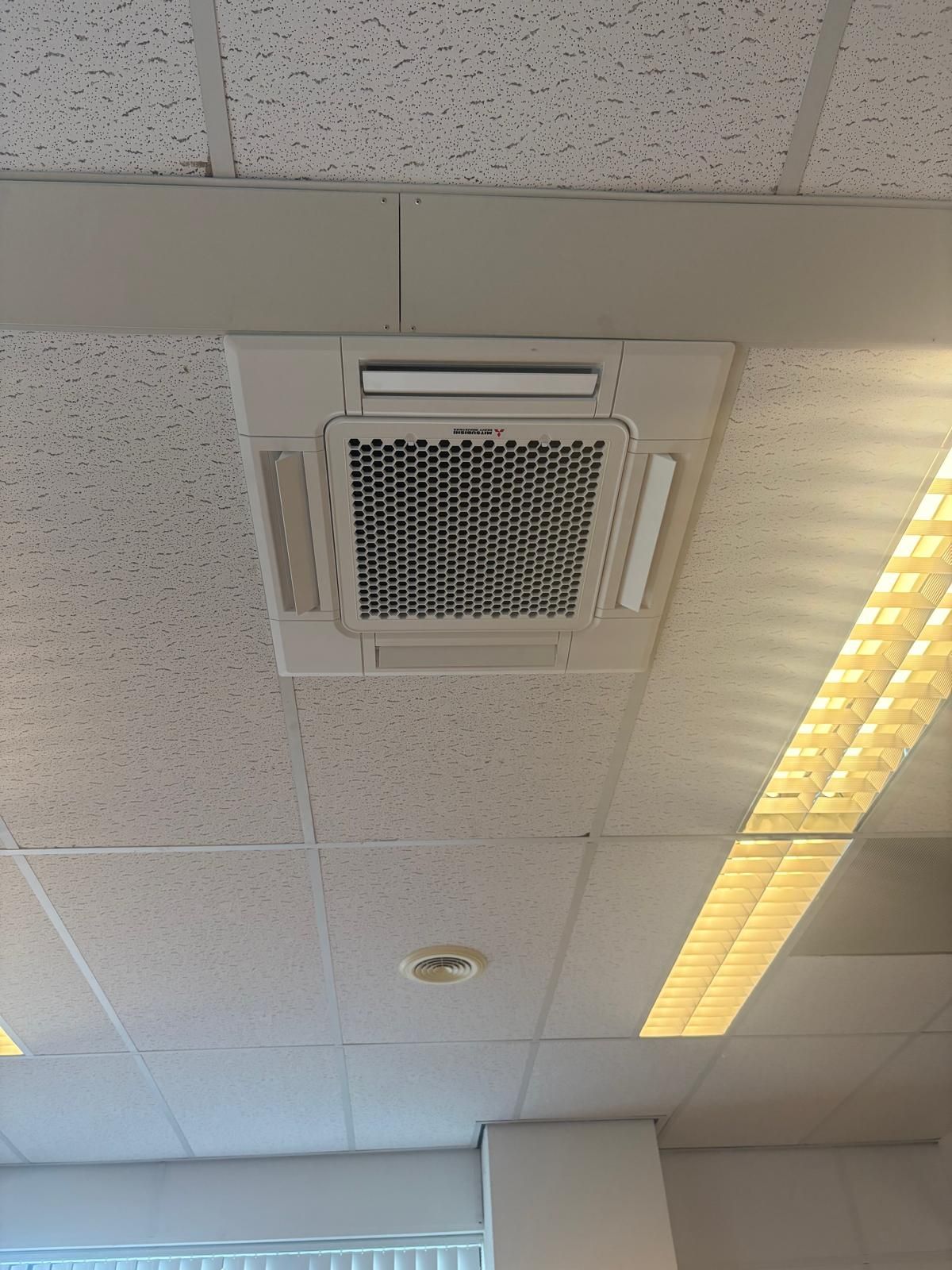 Plafondairconditioningunit gemonteerd op een rasterplafond in een kantooromgeving.