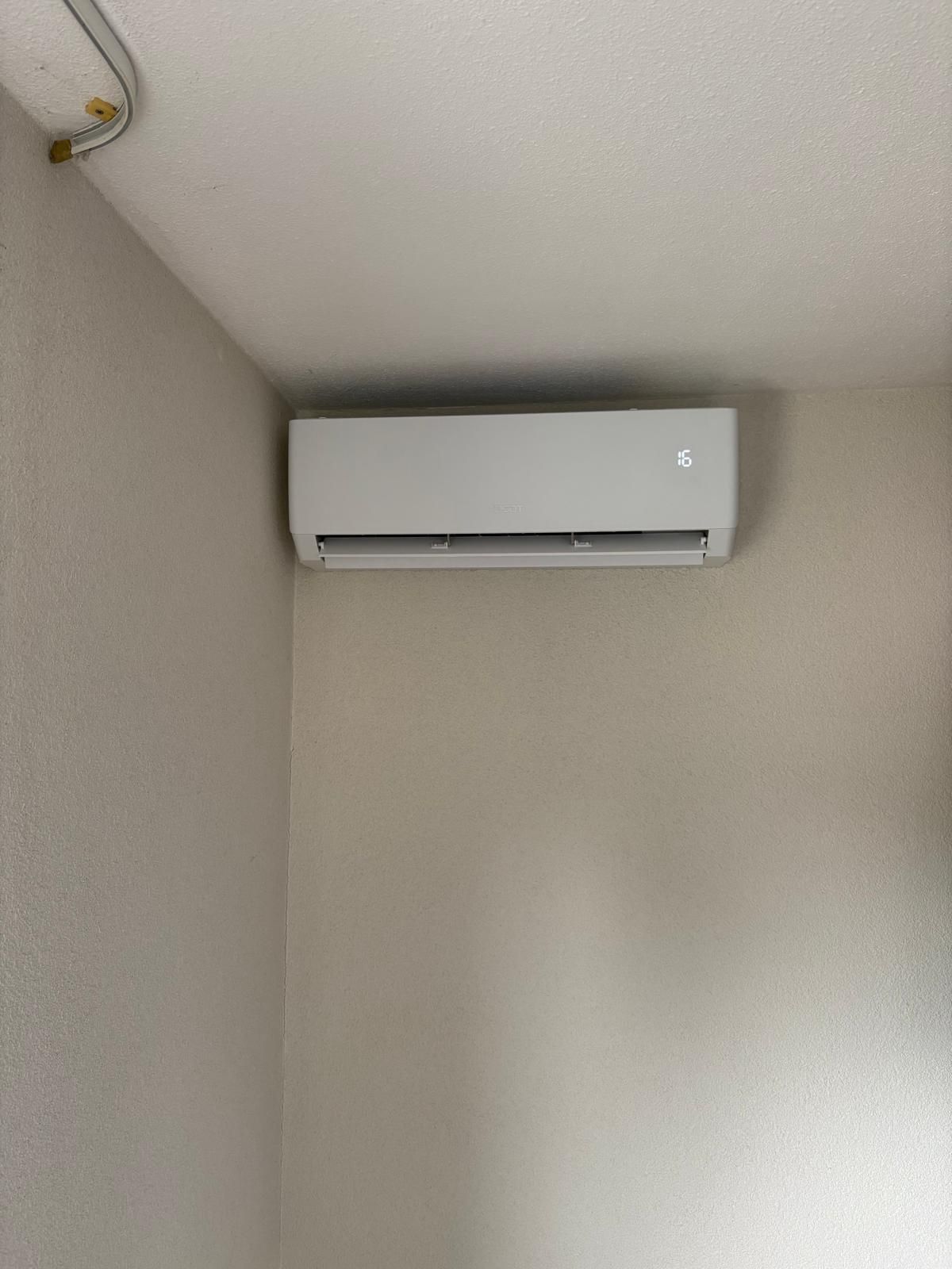 Witte, aan de muur gemonteerde airconditioningunit op een beige muur, vlakbij een plafond met een leiding.