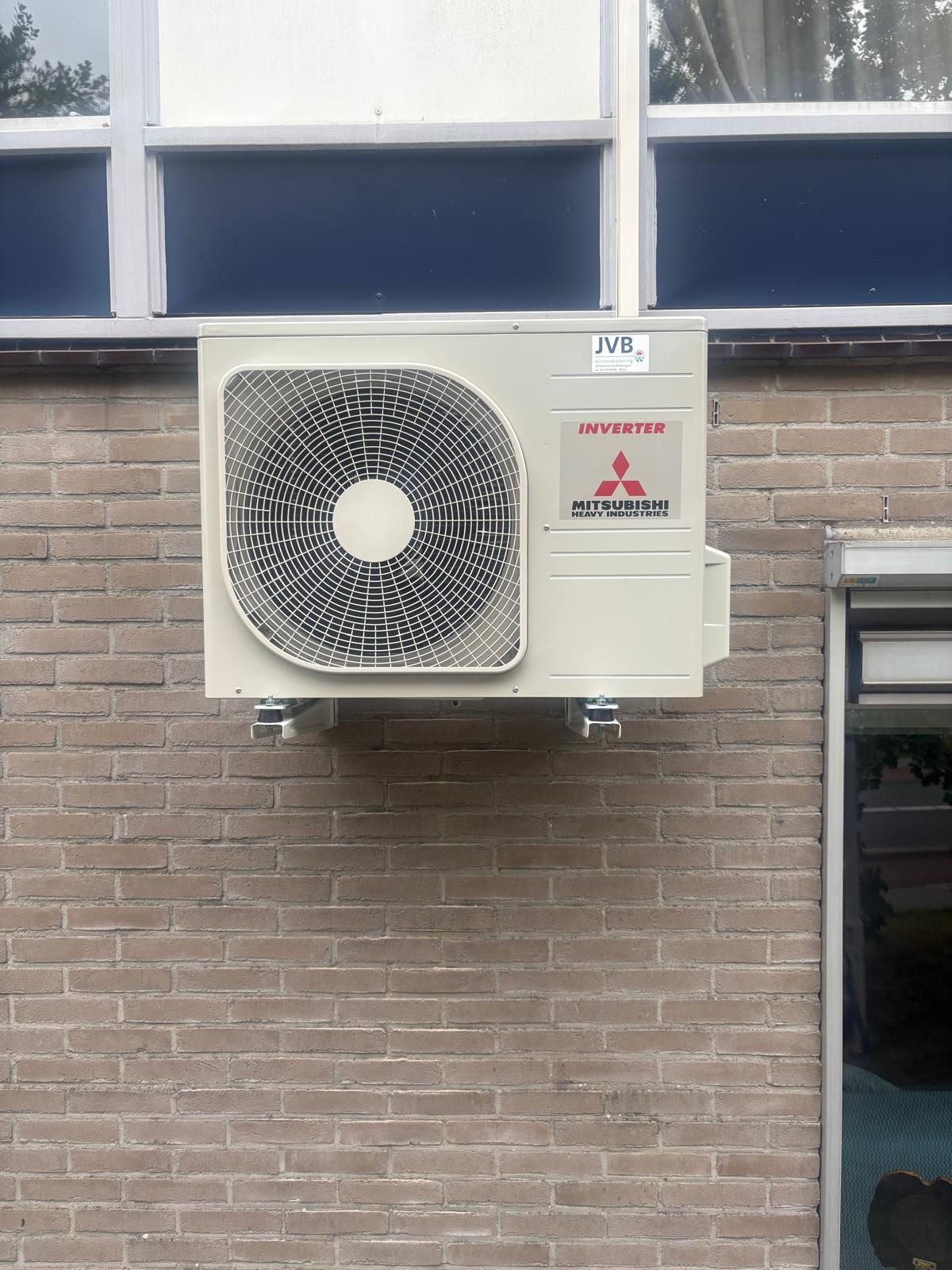 Een Mitsubishi airconditioner is gemonteerd aan een bakstenen muur, onder een raam.
