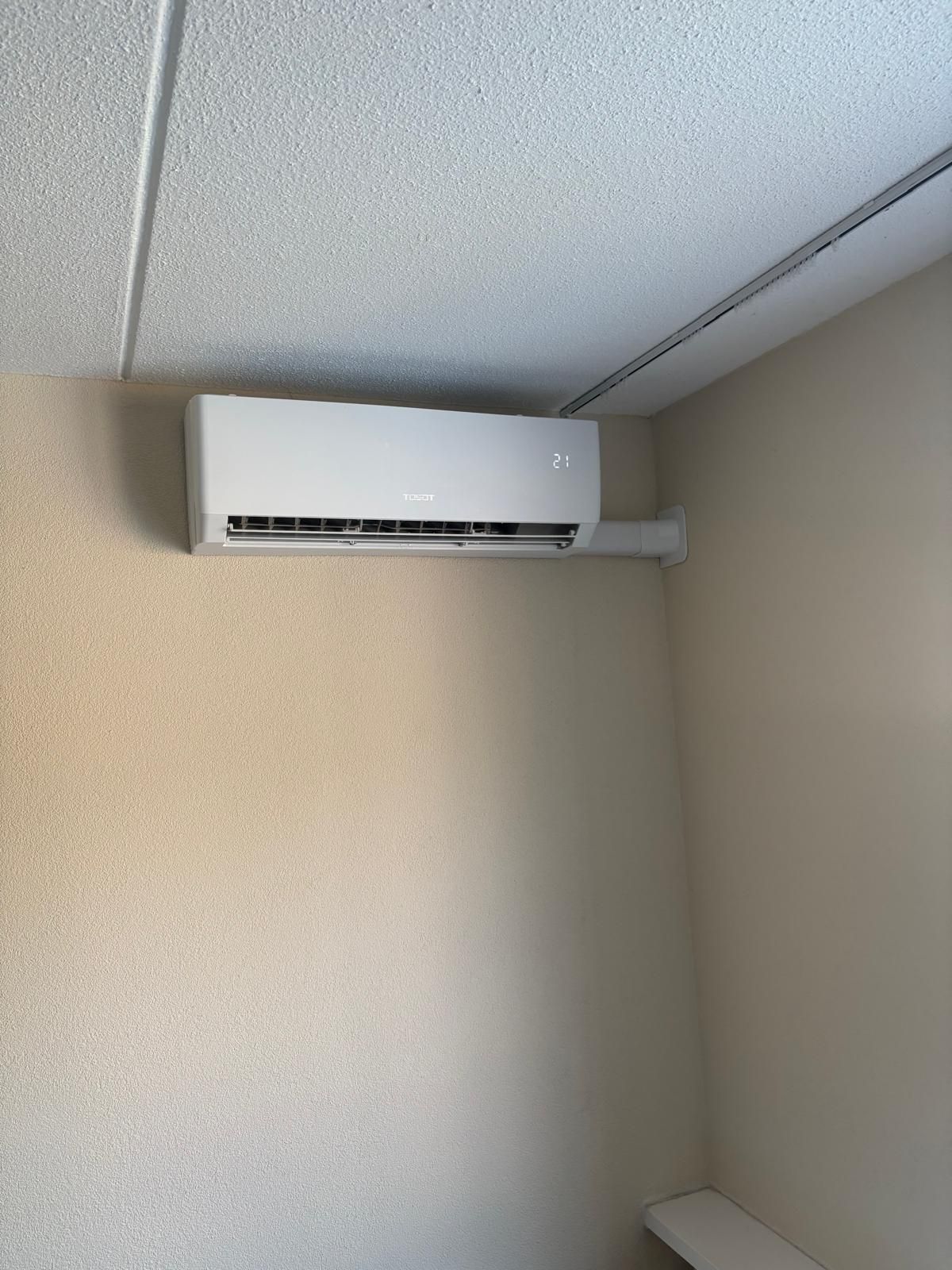Witte airconditioningunit gemonteerd aan een beige muur in een hoek.
