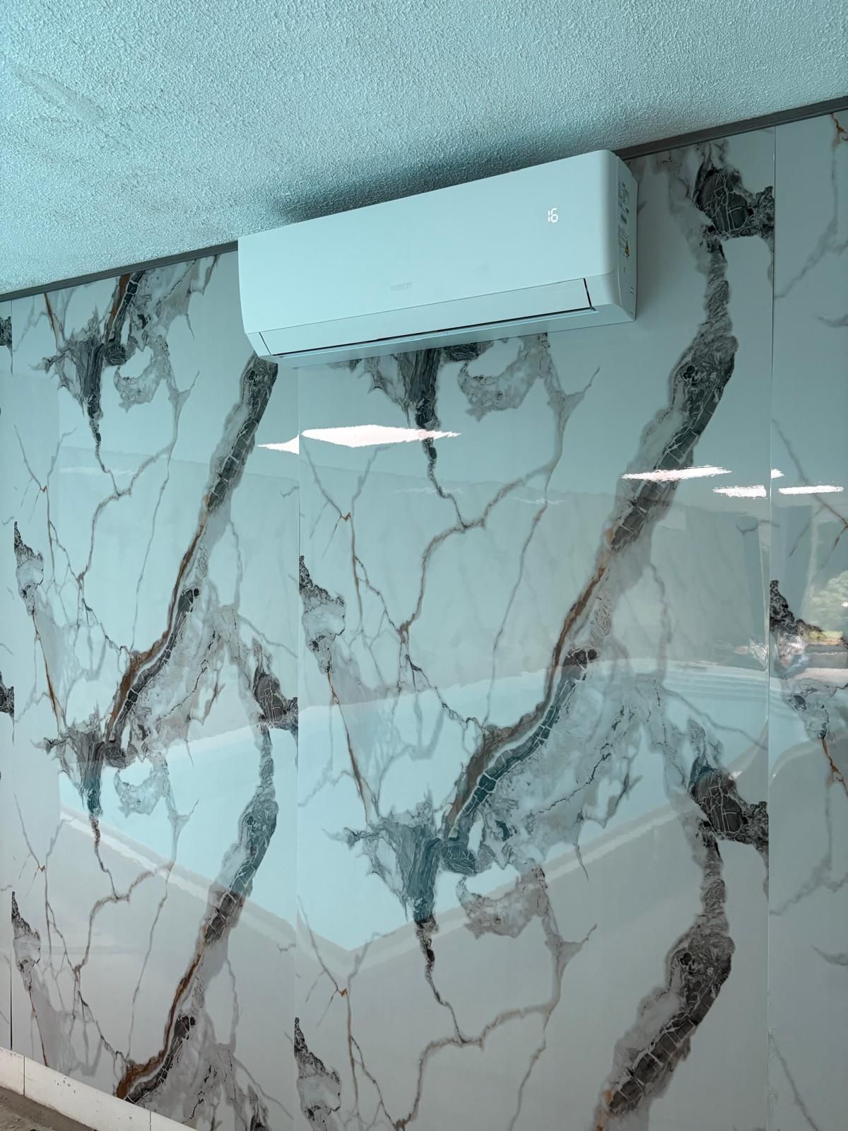 Witte airconditioner gemonteerd aan een muur met marmerpatroon.