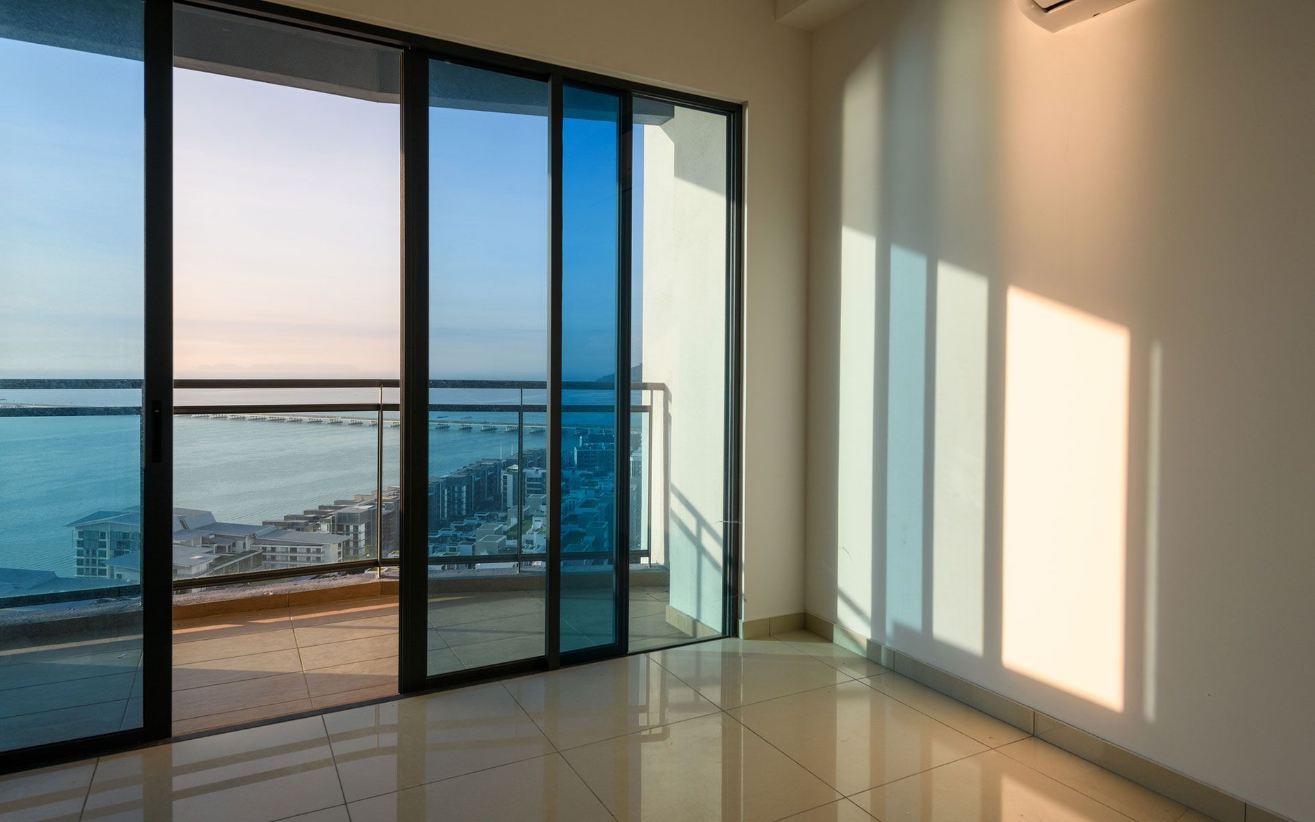 An empty room with sliding glass doors leading to a balcony overlooking the ocean.