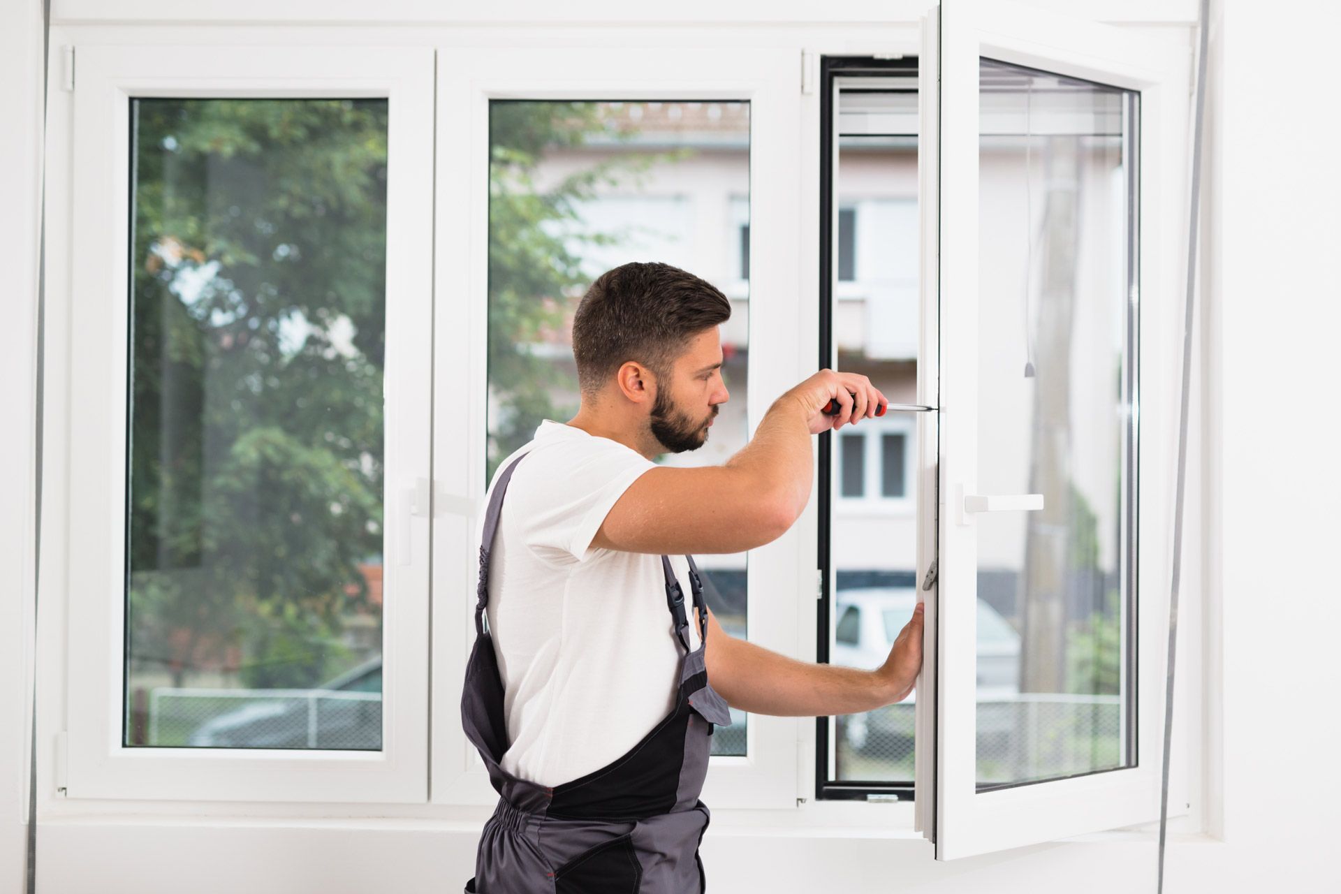 A technician adjusting a white window frame with a screwdriver during residential window repair