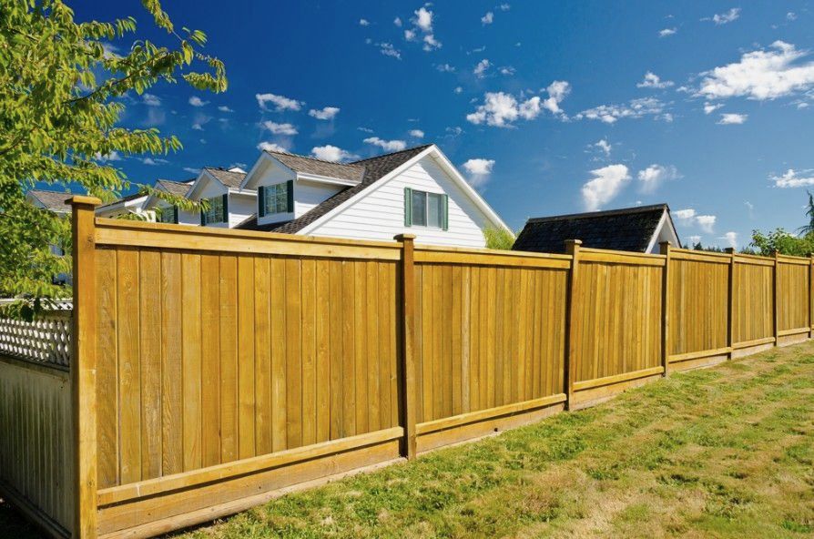A Wooden Fence Surrounds A Lush Green Yard In Front Of A House — CQ Fencing & Retaining Walls In Tannum Sands, QLD